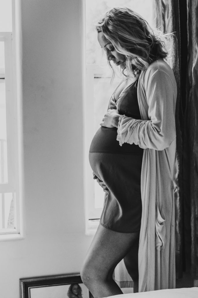 Black and white photograph of a pregnant woman in her bedroom in Los Angeles, CA
