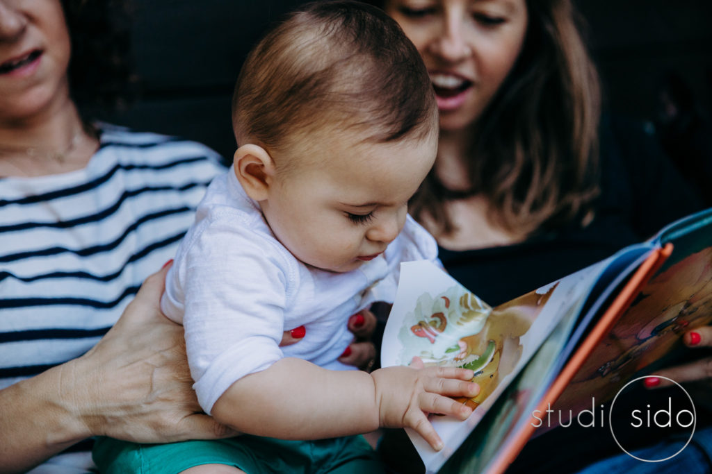 Baby sits on parents' laps and crumples pages of a book, Silver Lake, Los Angeles, CA