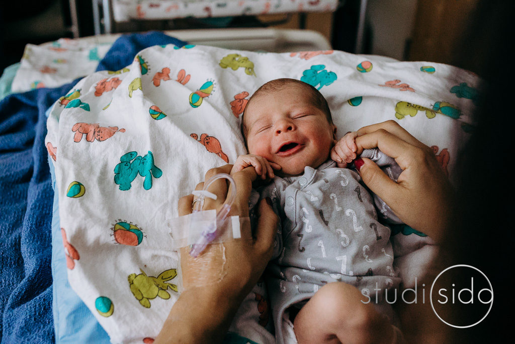 Newborn baby smiles while holding fingers. Fresh 48 session Kaiser Hospital Hollywood.