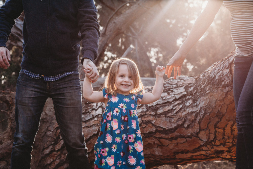 Little girl smiles while holding her parents' hands