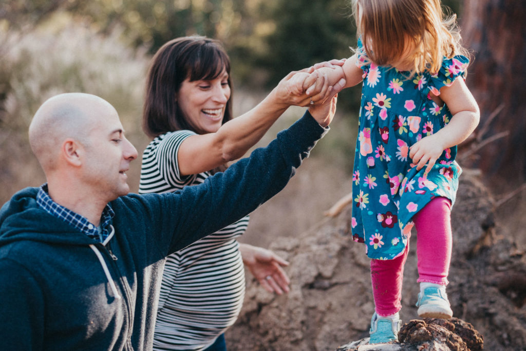 Young girl climbs on tree while holding parents' hands