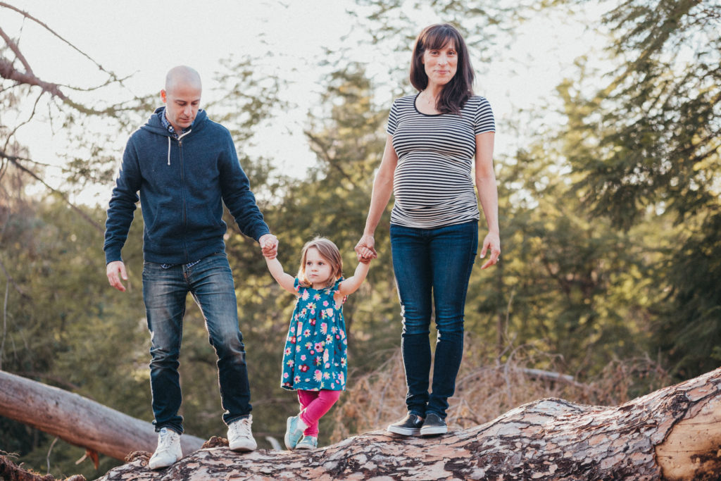 Mom, dad, and young daughter all stand on a log in Griffith Park, Los Angeles, CA