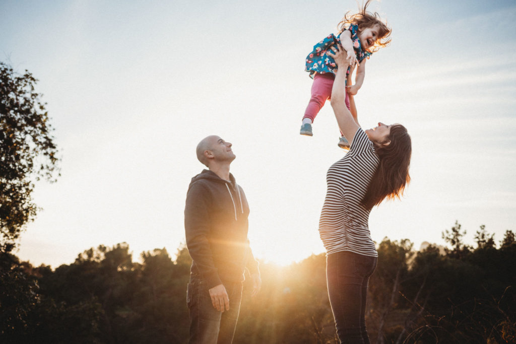 Mom lifts her daughter high in the air while dad looks on