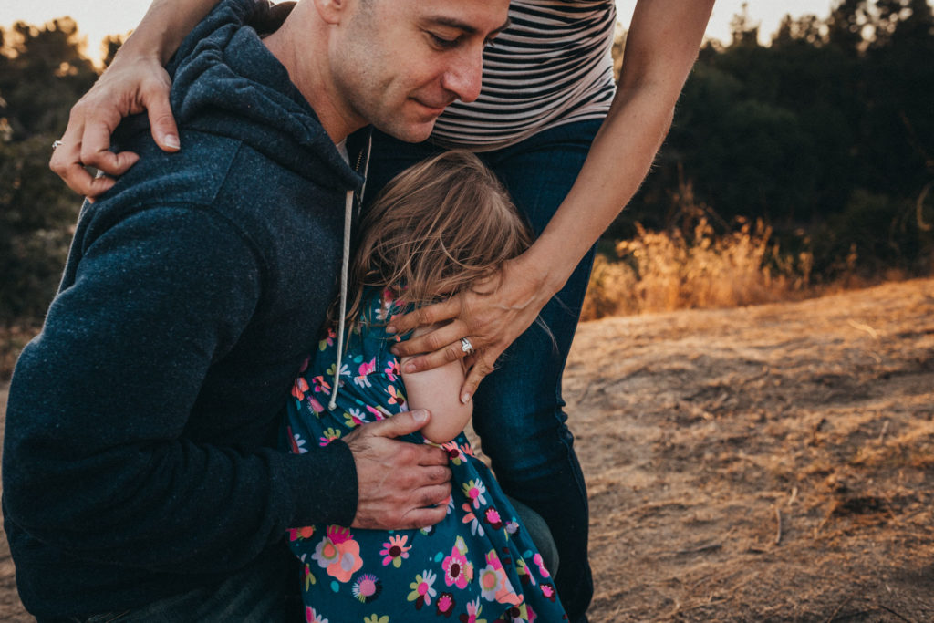 a close up photograph of mom and dad's arms around their daughter