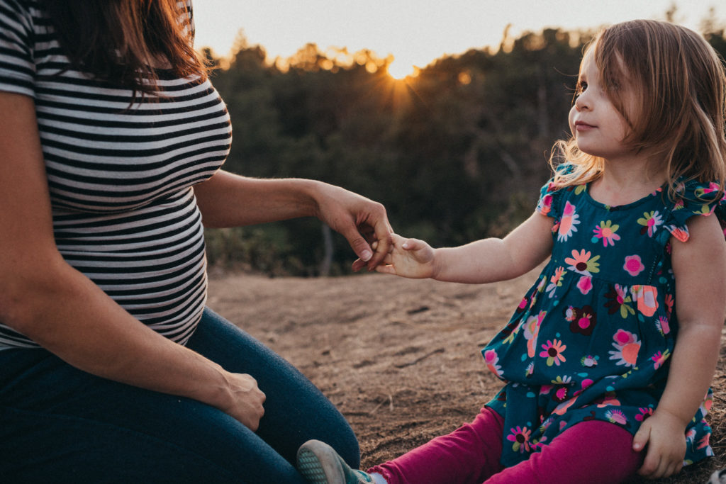 Daughter looks at mom and holds hand at sunset