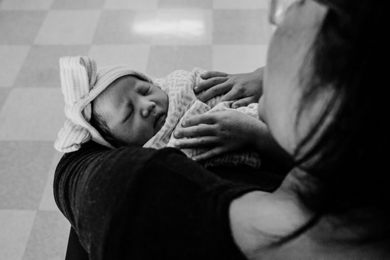 A black and white photograph of a little boy's hands on his newborn sister's chest